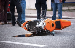 Orange motorcycle on the ground after a collision with onlookers and police officers present